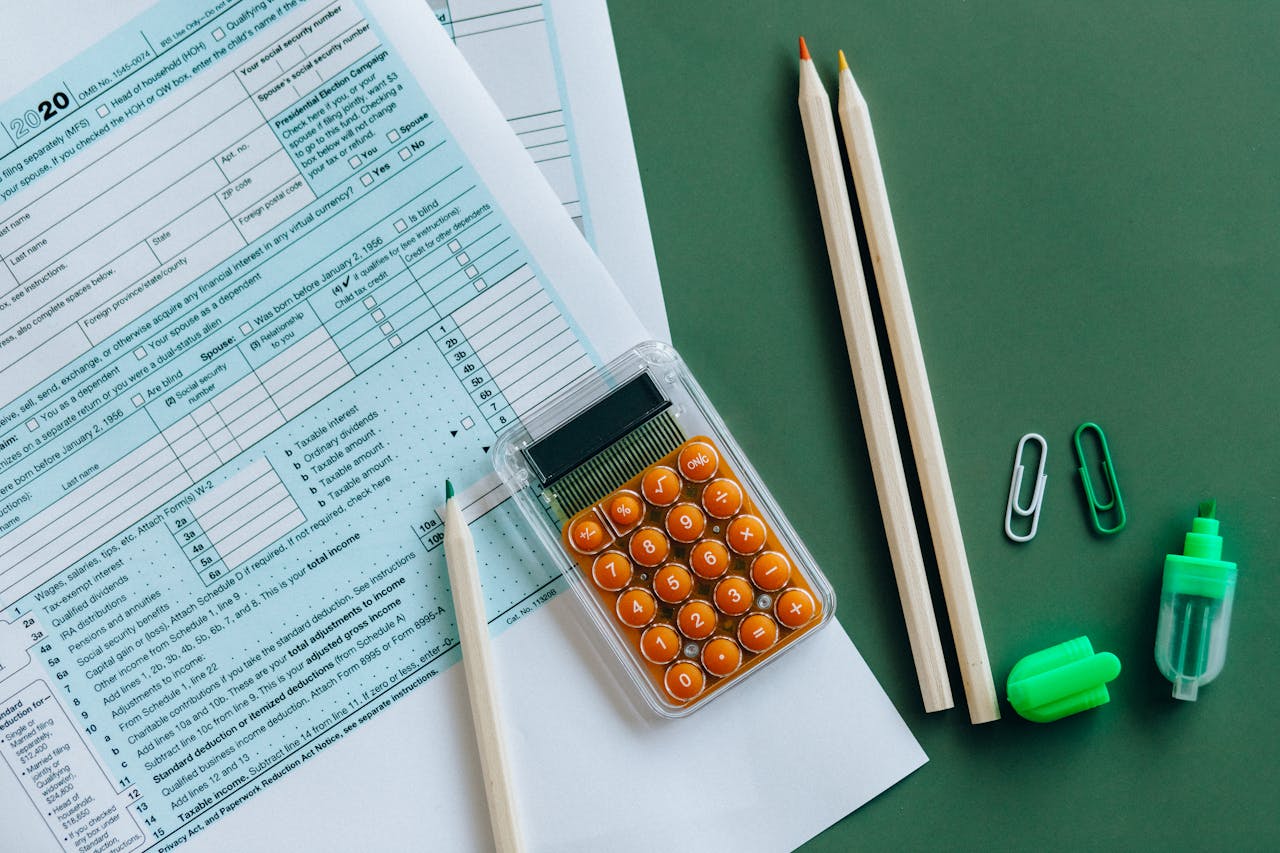 Flat lay of tax forms, calculator, pencils, and clips on green surface, ideal for finance or accounting themes.